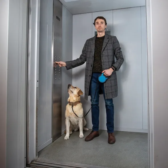 Handsome stylish man standing with labrador dog in elevator