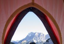 Dog sitting outside pitched tent with Tent Seebensee in background