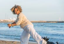 Woman playing with her dog on the beach while the dog bites her pants