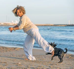 Woman playing with her dog on the beach while the dog bites her pants
