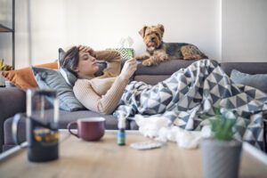 Woman lying sick on sofa with her dog