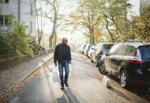 A fit older man walks a small dog white dog down neighborhood streets.