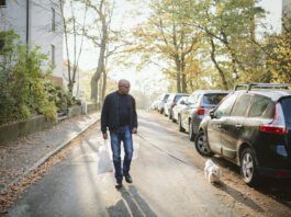 A fit older man walks a small dog white dog down neighborhood streets.