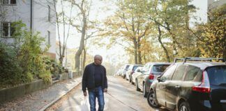 A fit older man walks a small dog white dog down neighborhood streets.