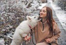 Young woman in winter park with white puppy. Woman with white Swiss shepherd