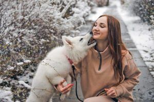 Young woman in winter park with white puppy. Woman with white Swiss shepherd